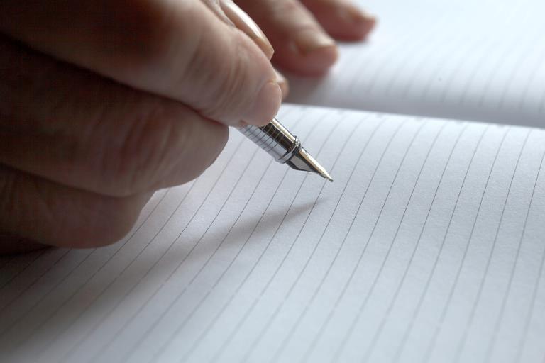 En hånd der holder en blæk pen mod linjeret papir