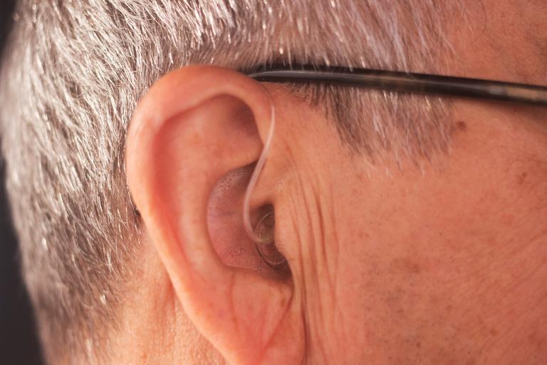 Et øre med en brillestang bagved og en slange til høreapparat 