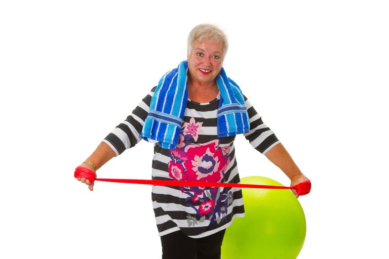En kvinde med en træningsbold og en træningselastik og et håndklæde over skuldrene